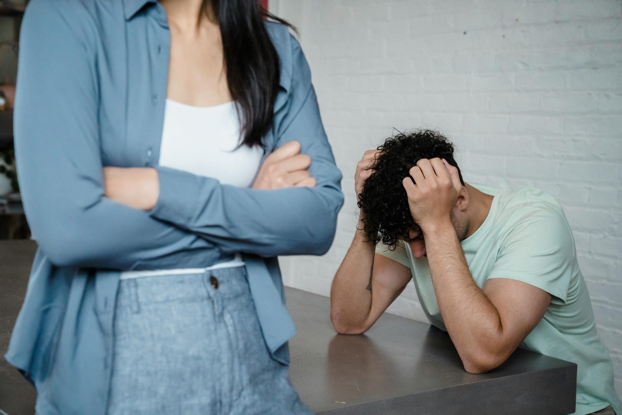 Man sitting at desk with head in hands, body of woman standing in front of him with arms crossed