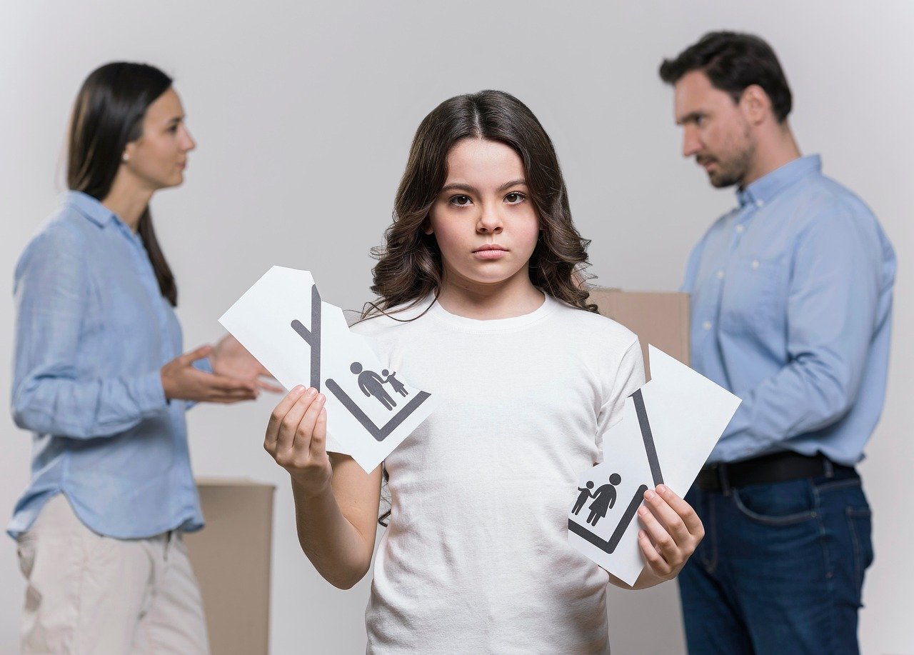 Young girl holding two halves of paper with sticker figure family and home in front of arguing parents