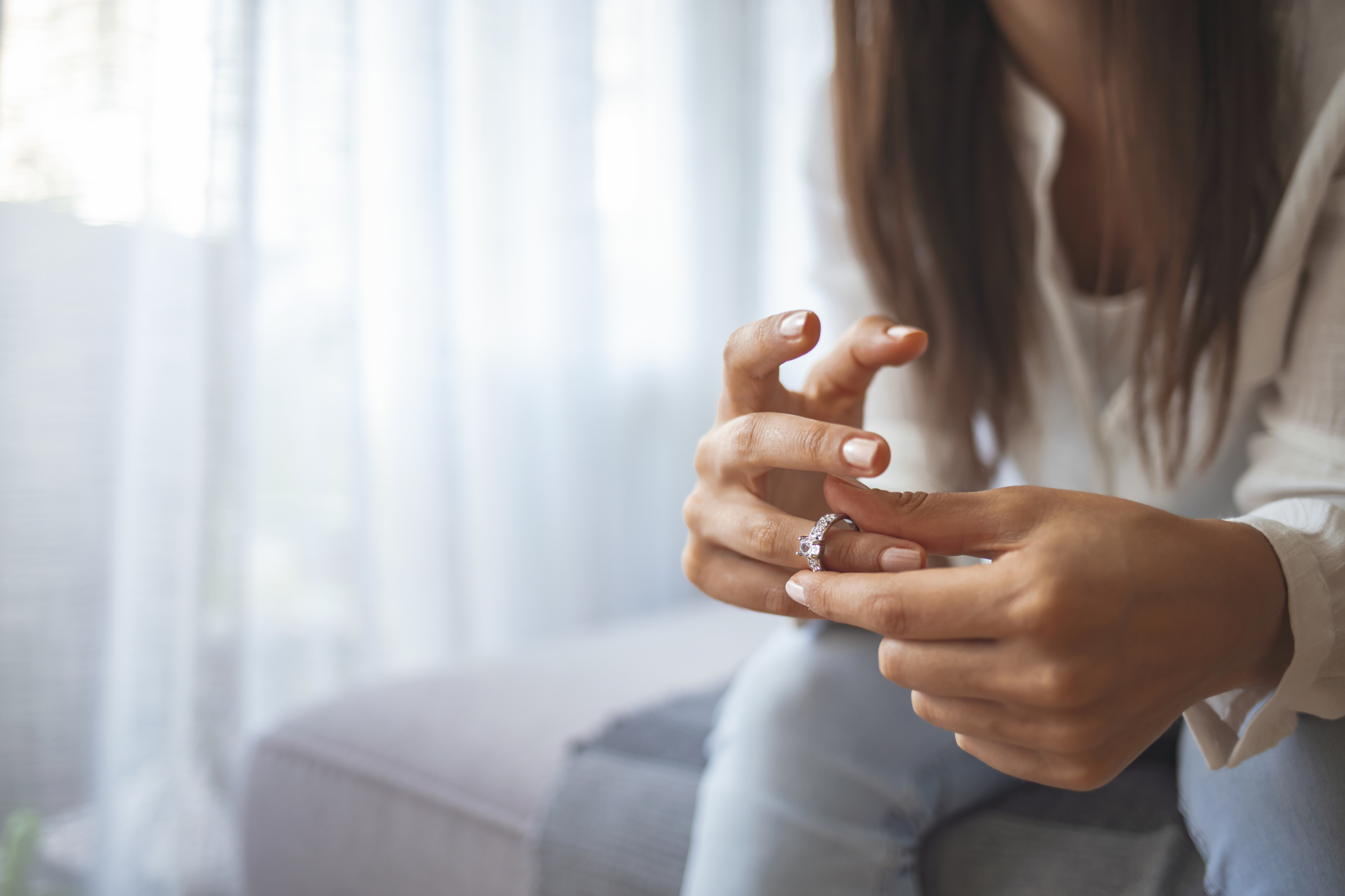 Body of woman sitting on couch alone taking off wedding ring