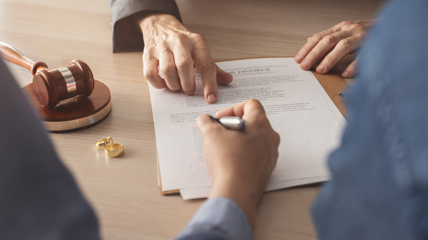 Bodies of two people signing divorce papers, with hands of lawyer showing where to sign