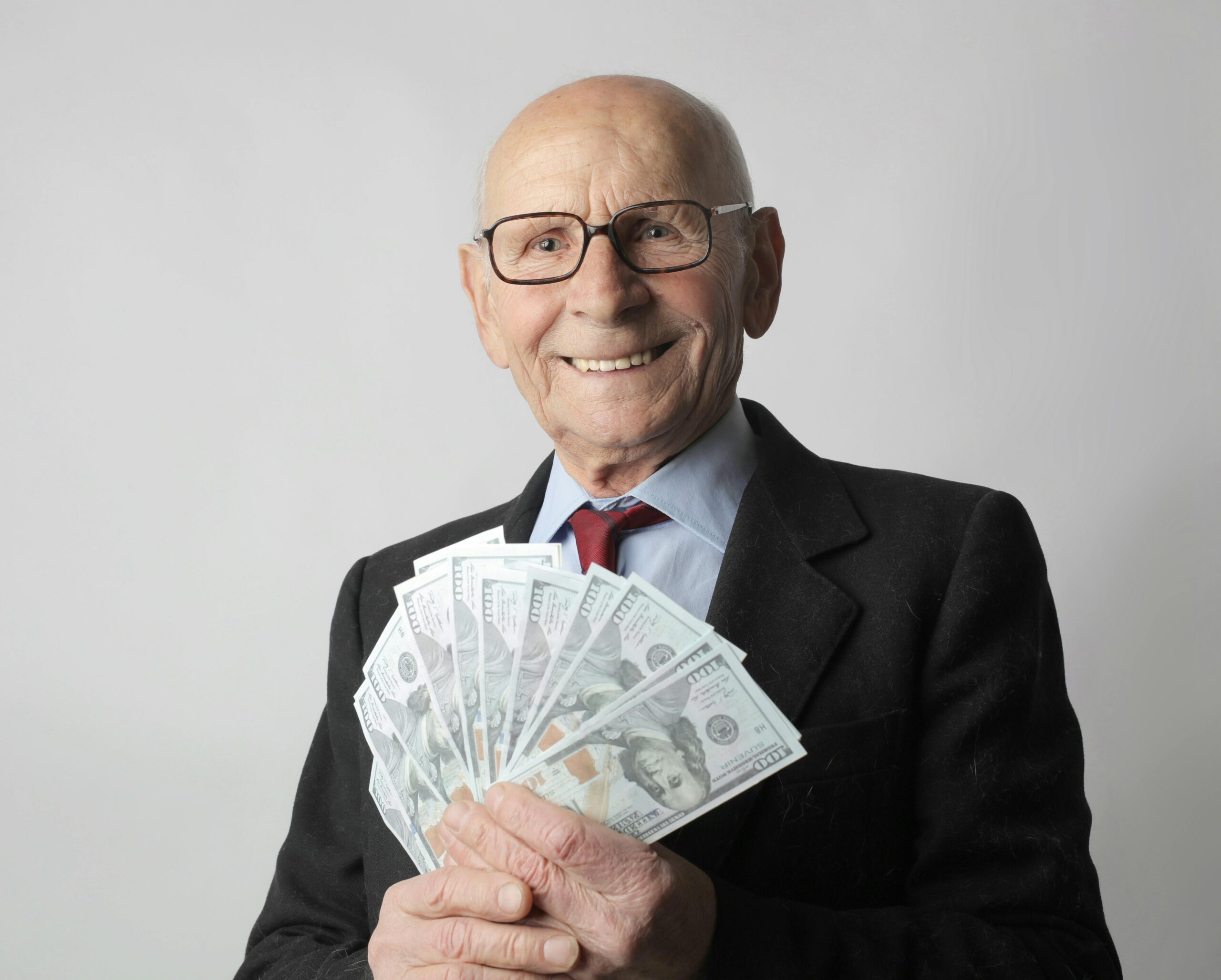 Old man in glasses and suit, smiling with handful of fanned out money