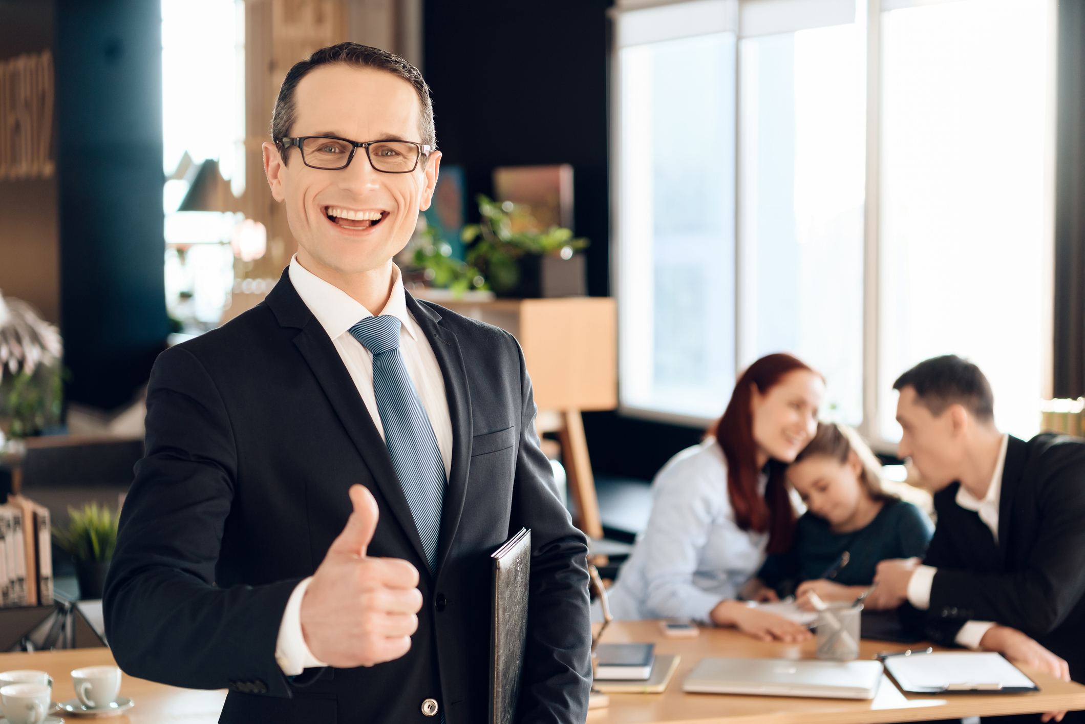 Man in suit and glasses giving a thumbs up in lawyer's office with parents and child behind him